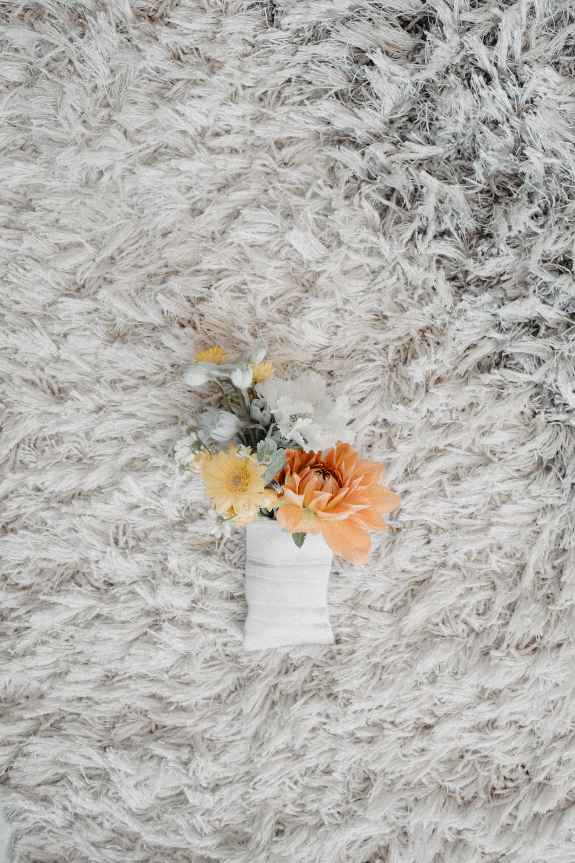 Small white vase with orange and yellow flowers on a fluffy white rug