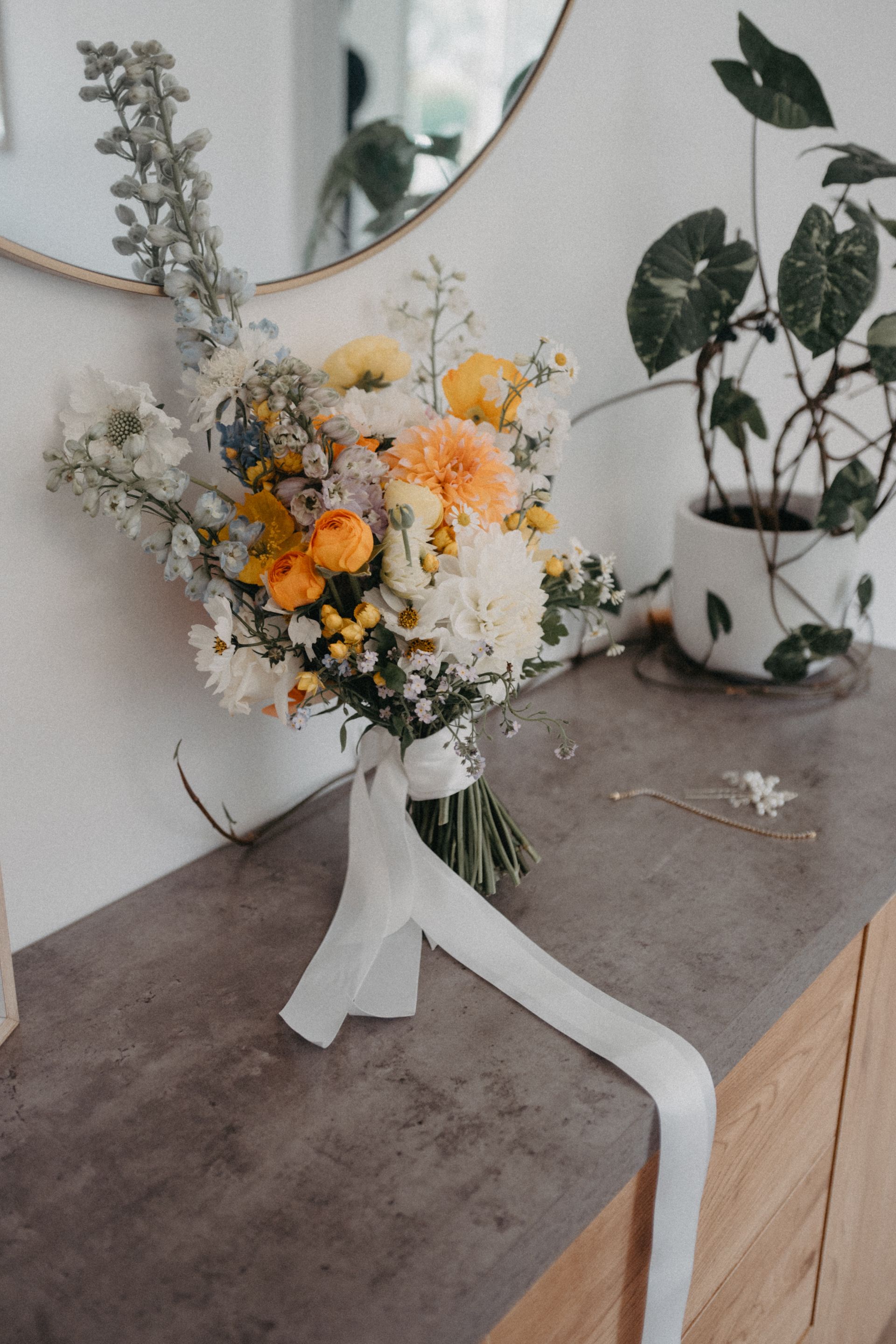 Small white bouquet with yellow and orange flowers on a tabletop beside a mirror