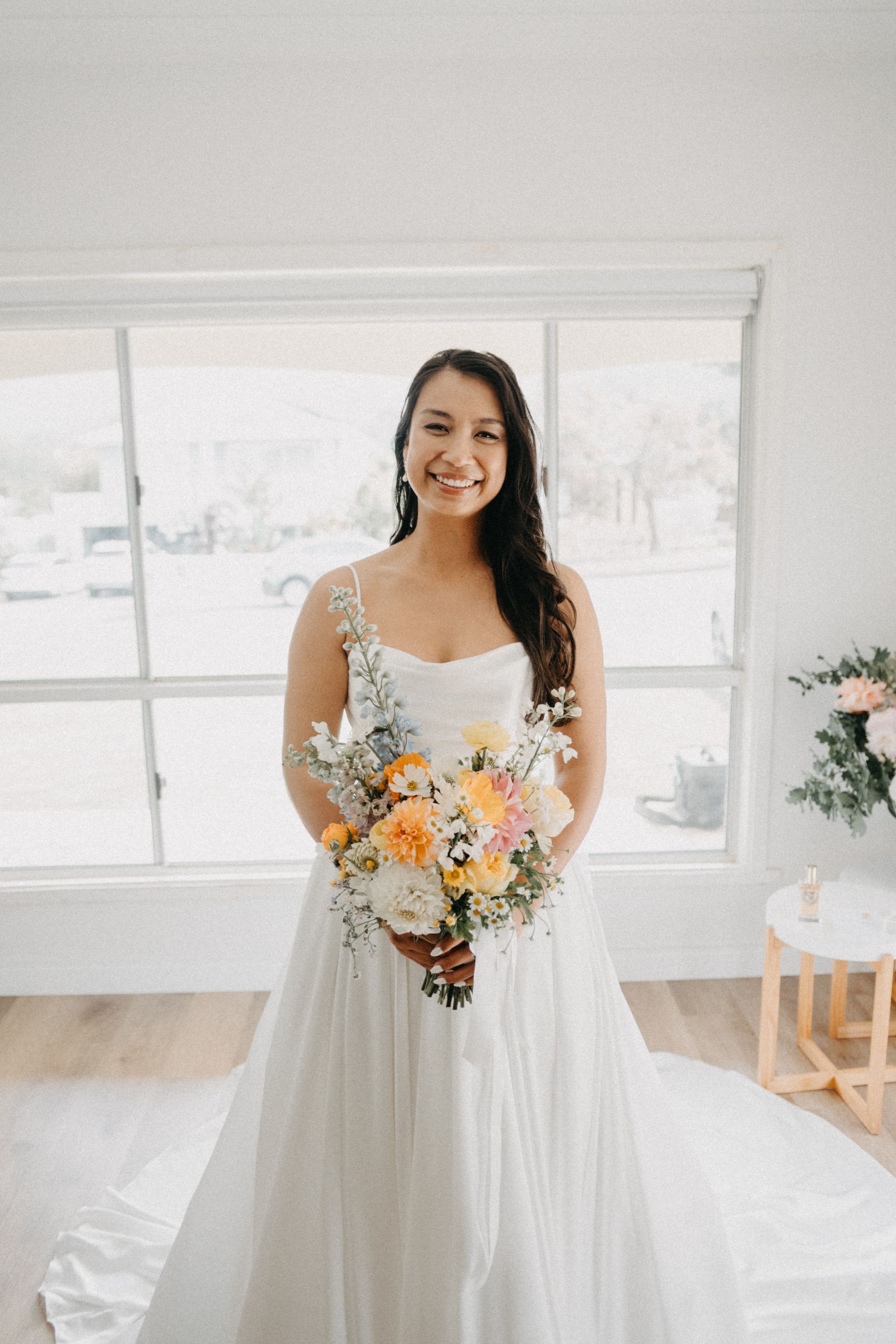 Woman in a white dress holding a bouquet of pastel flowers in a bright room