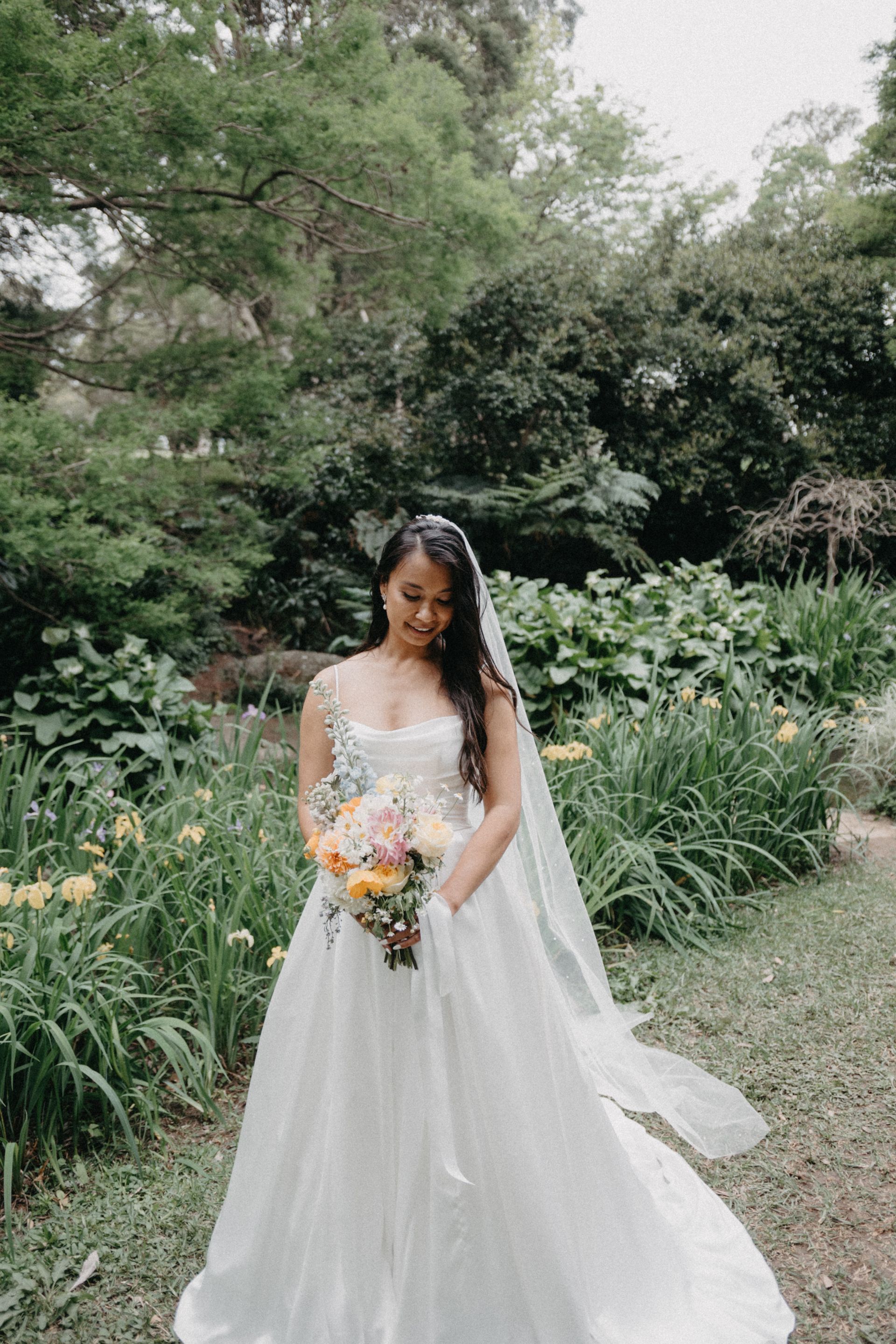 Bride in a white lace gown holding a bouquet in a lush garden setting