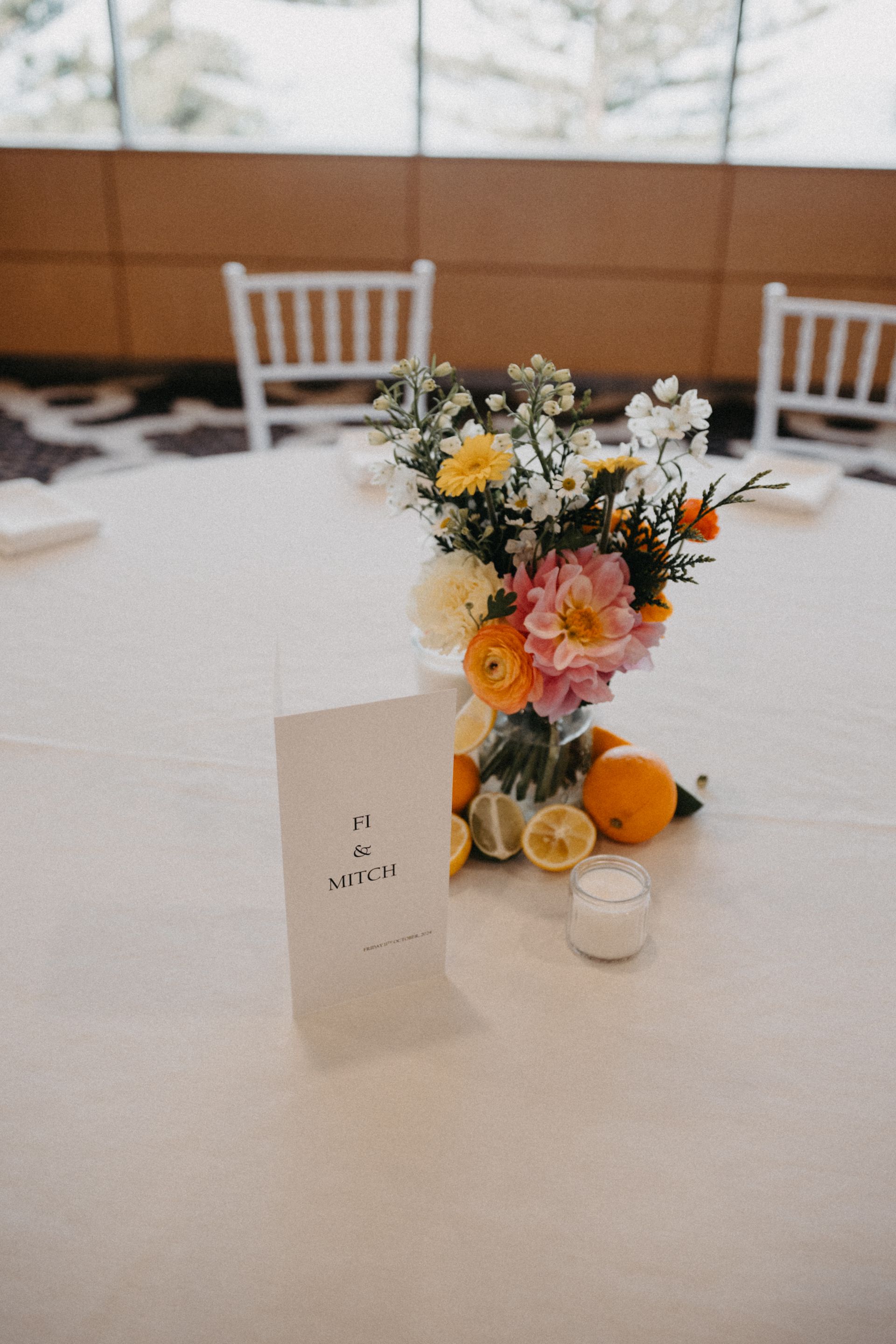 Small floral centerpiece with oranges and a table card on a white dining table