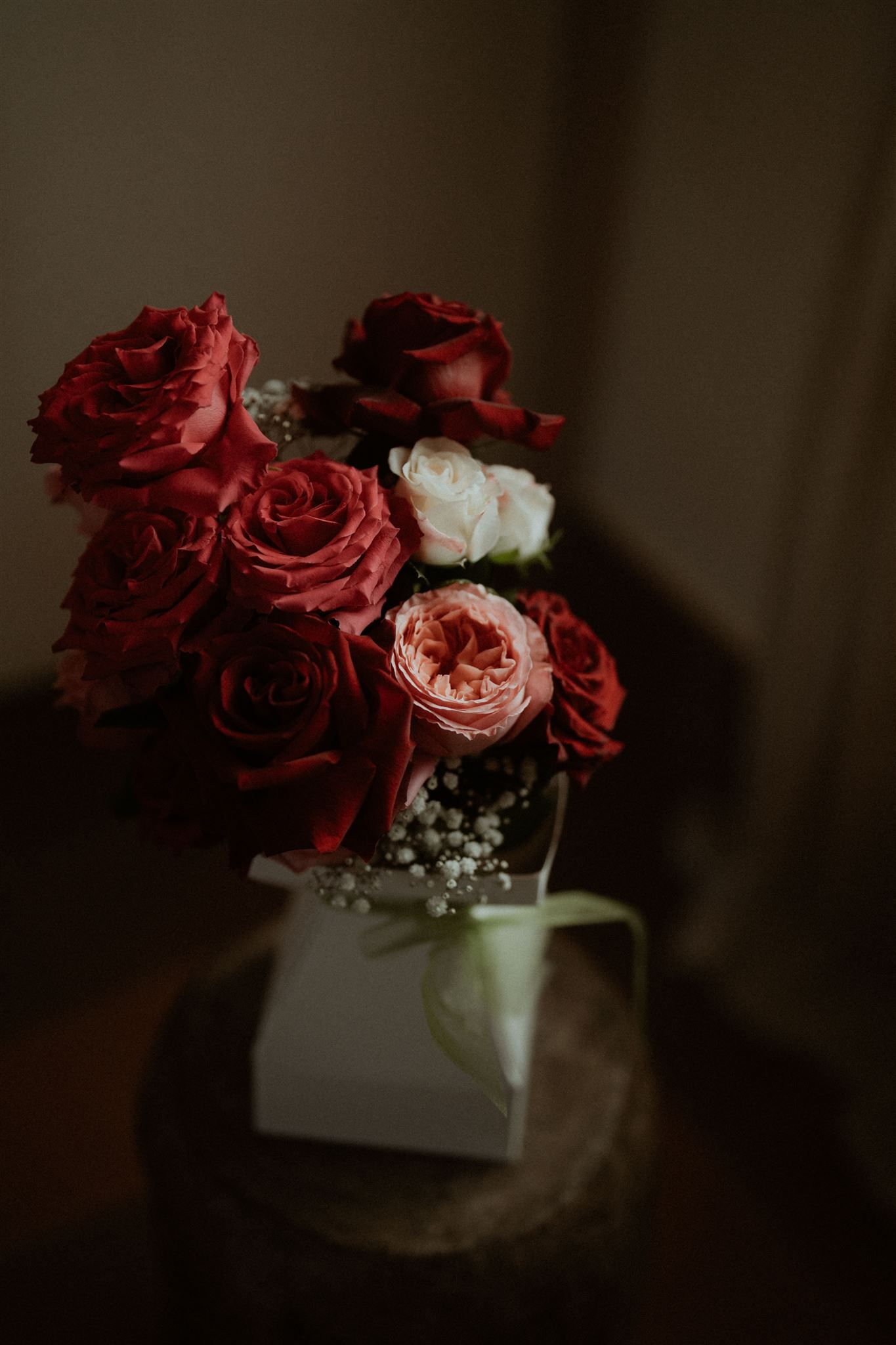 Red, white, and pink roses in a bouquet on a white pedestal against a dark background