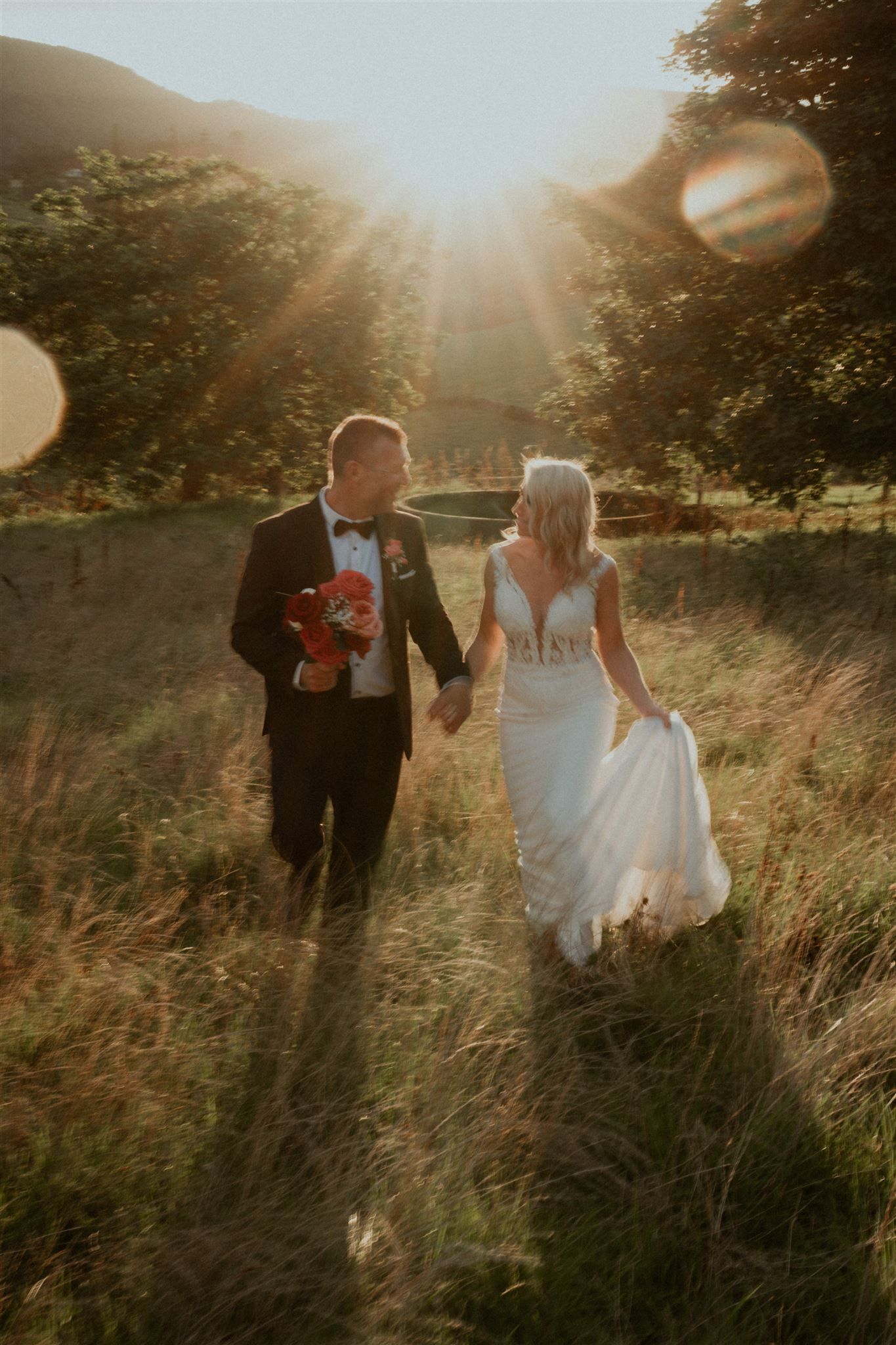 Bride and groom walking hand in hand through a sunlit field at golden hour