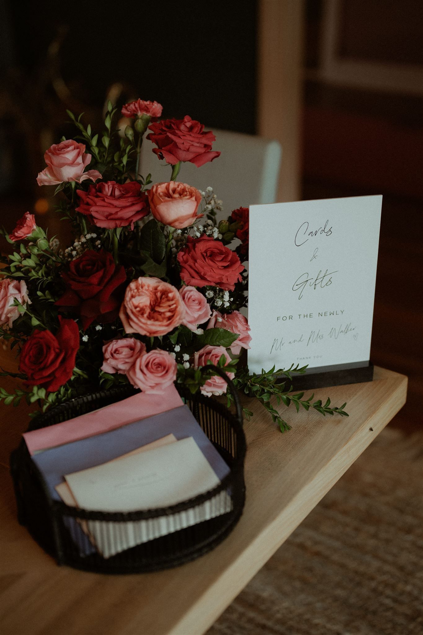 Pink flower bouquet with a greeting card and a black basket on a wooden table