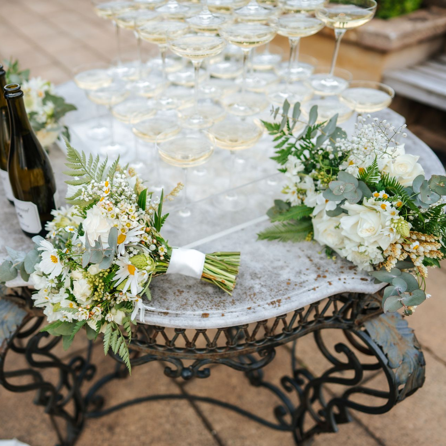 Wedding reception table with champagne glasses and white floral arrangements on an ornate wrought-iron stand