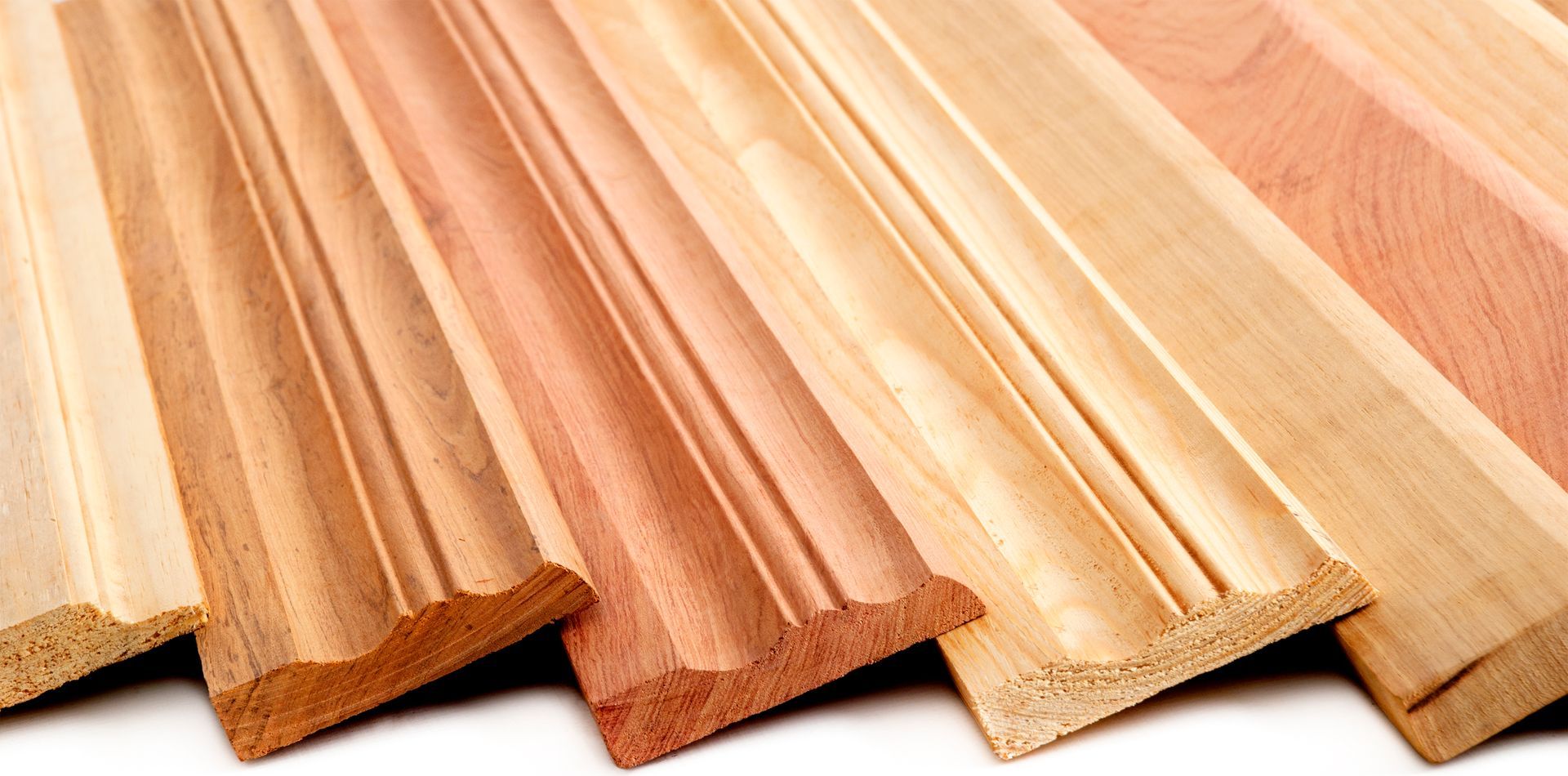 A group of wooden molding pieces are stacked on top of each other on a white surface.