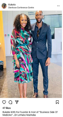 Woman in colorful dress and man in suit pose together at a conference center.