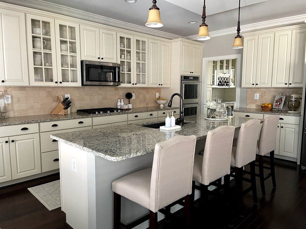 A kitchen with white cabinets , granite counter tops , and stools.
