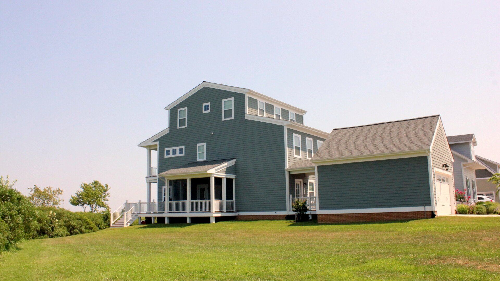 A large house with a porch and a garage is sitting on top of a lush green field.