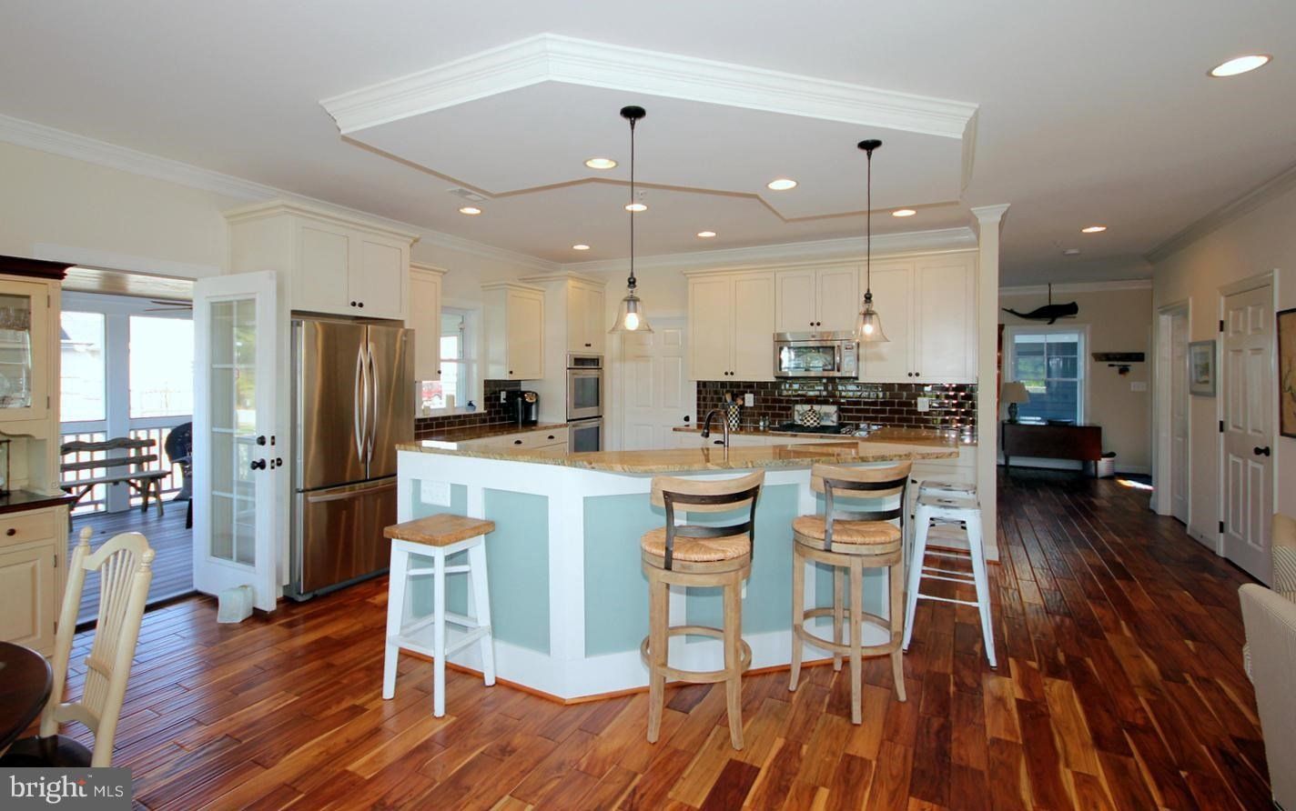 A kitchen with hardwood floors , white cabinets , stainless steel appliances and a large island.