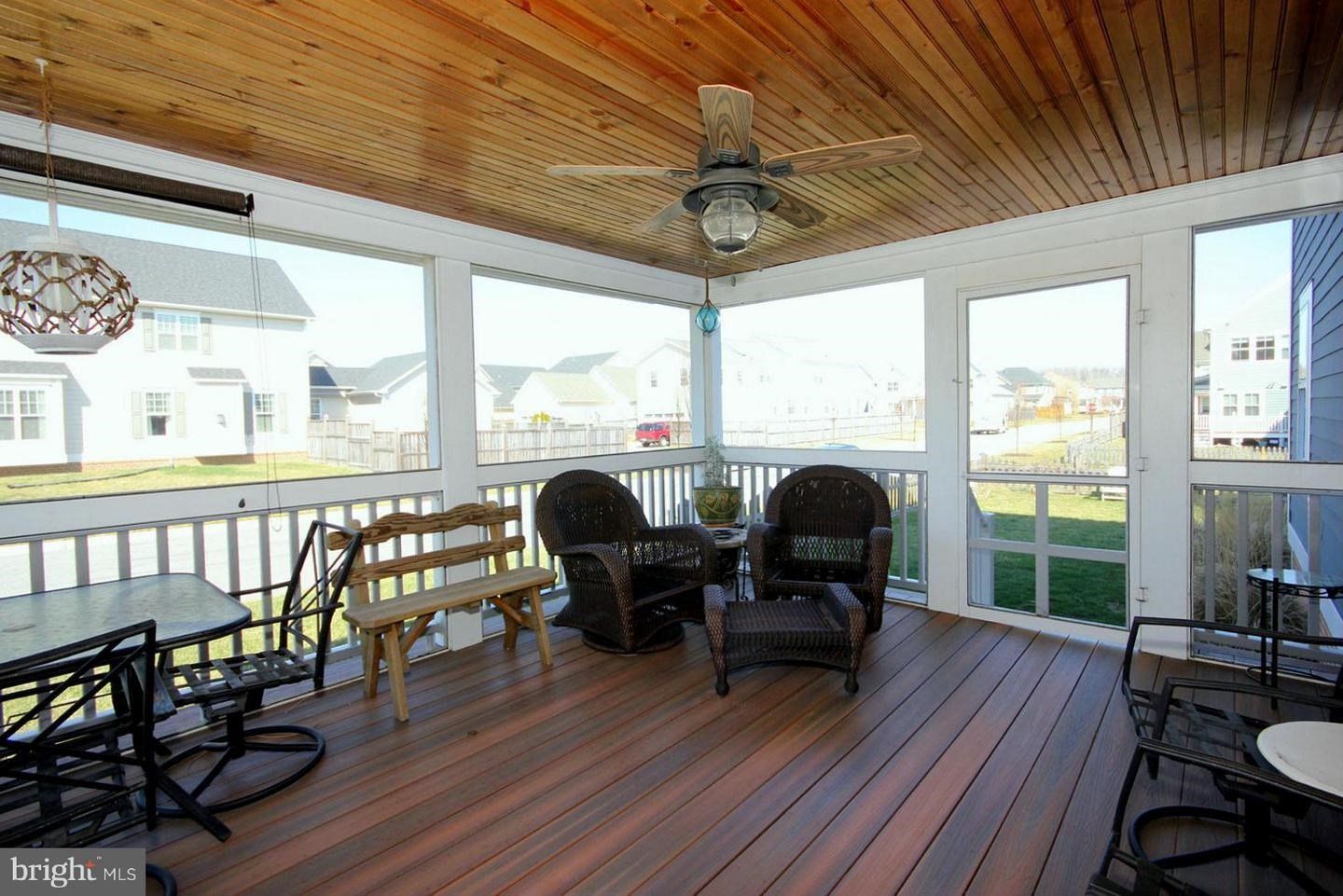 A screened in porch with chairs , a table and a ceiling fan.