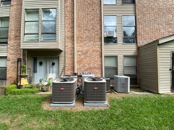 Brick apartment building exterior with two HVAC units, a side door, and a grassy lawn