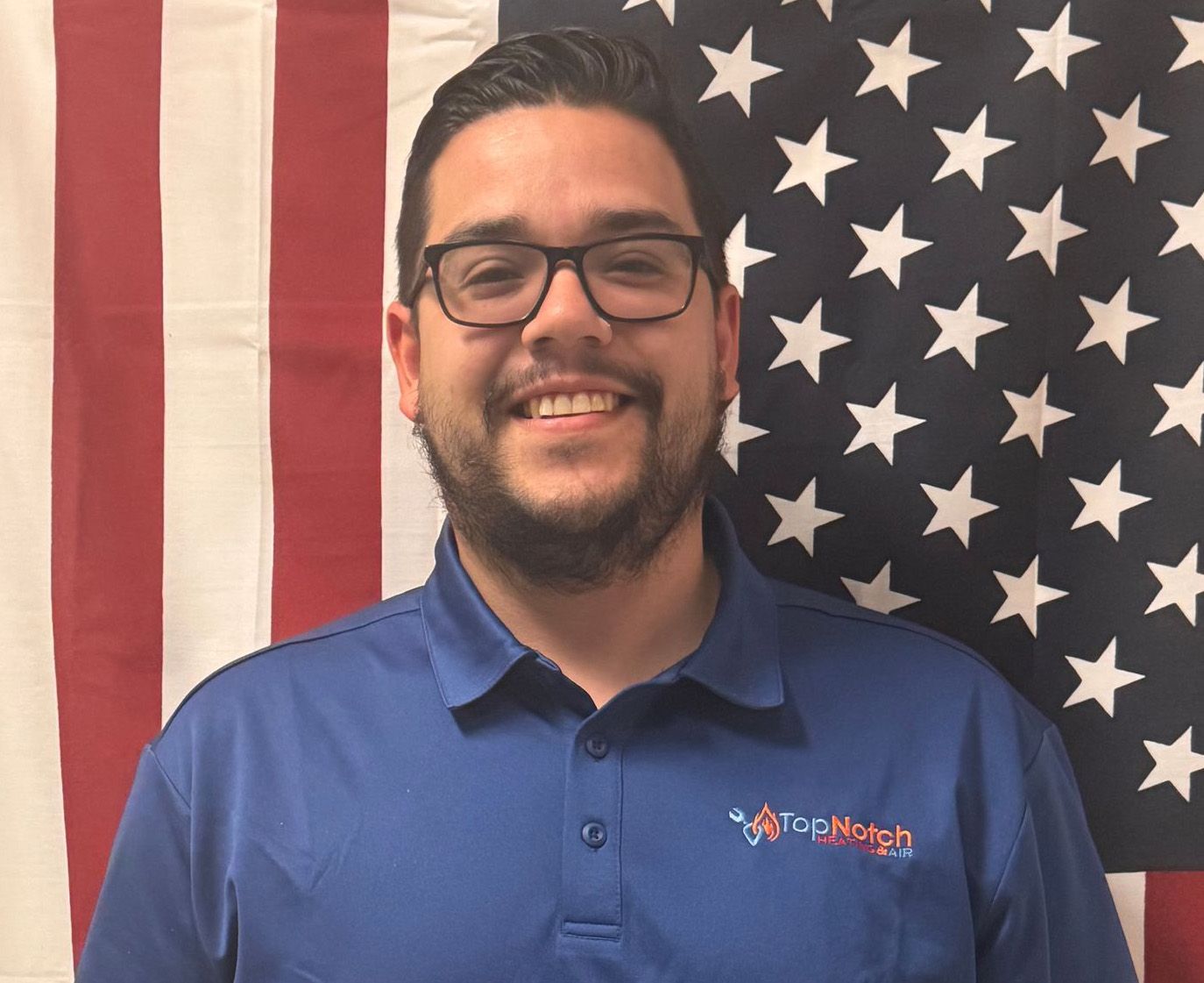 Smiling person in blue polo standing in front of an American flag backdrop