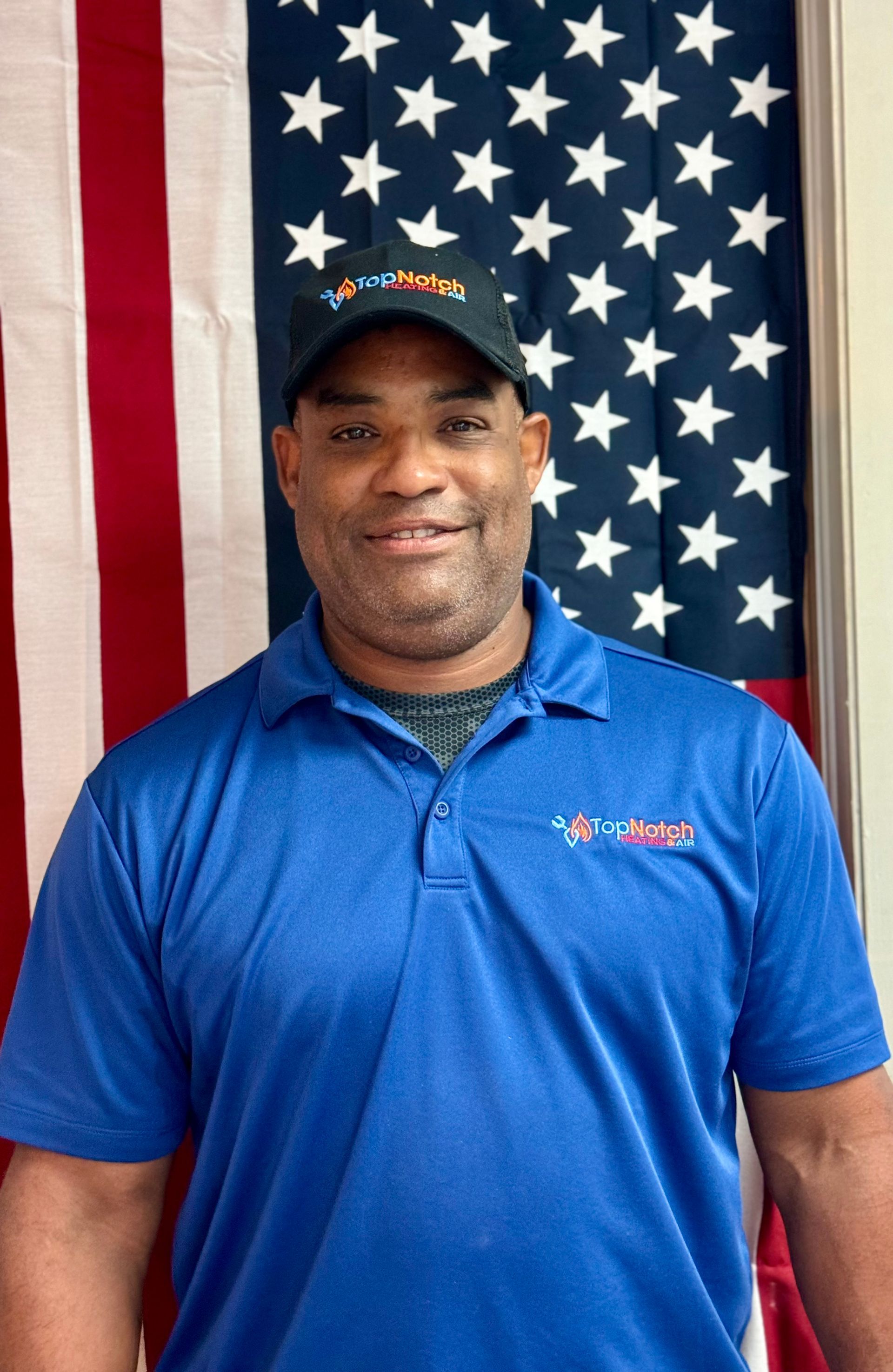 Man in blue polo and cap standing before an American flag backdrop