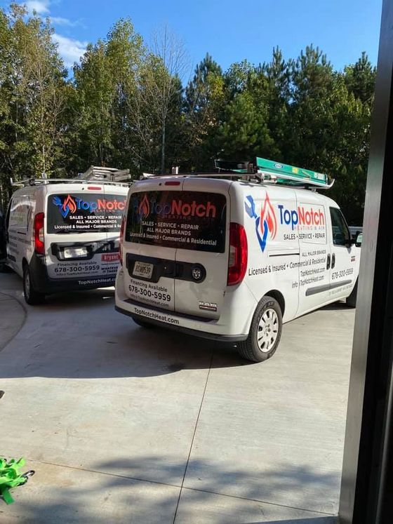 Two white Top Notch service vans parked in a sunny driveway beside trees