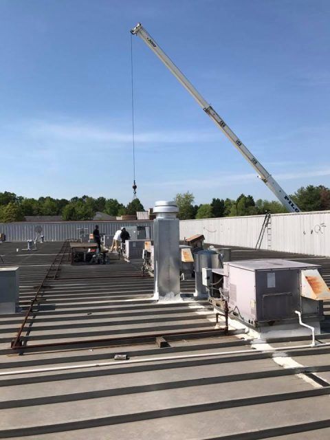 Rooftop construction site with crane, workers, and HVAC units under a blue sky