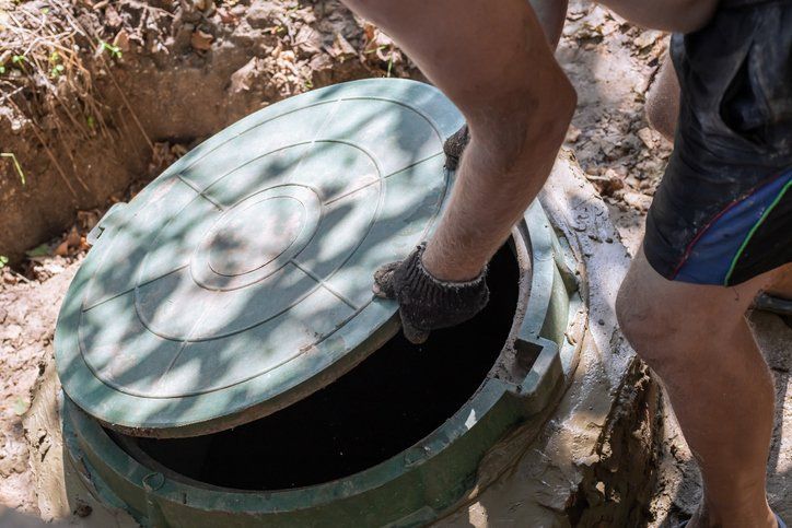 Person lifting a round green manhole cover outdoors