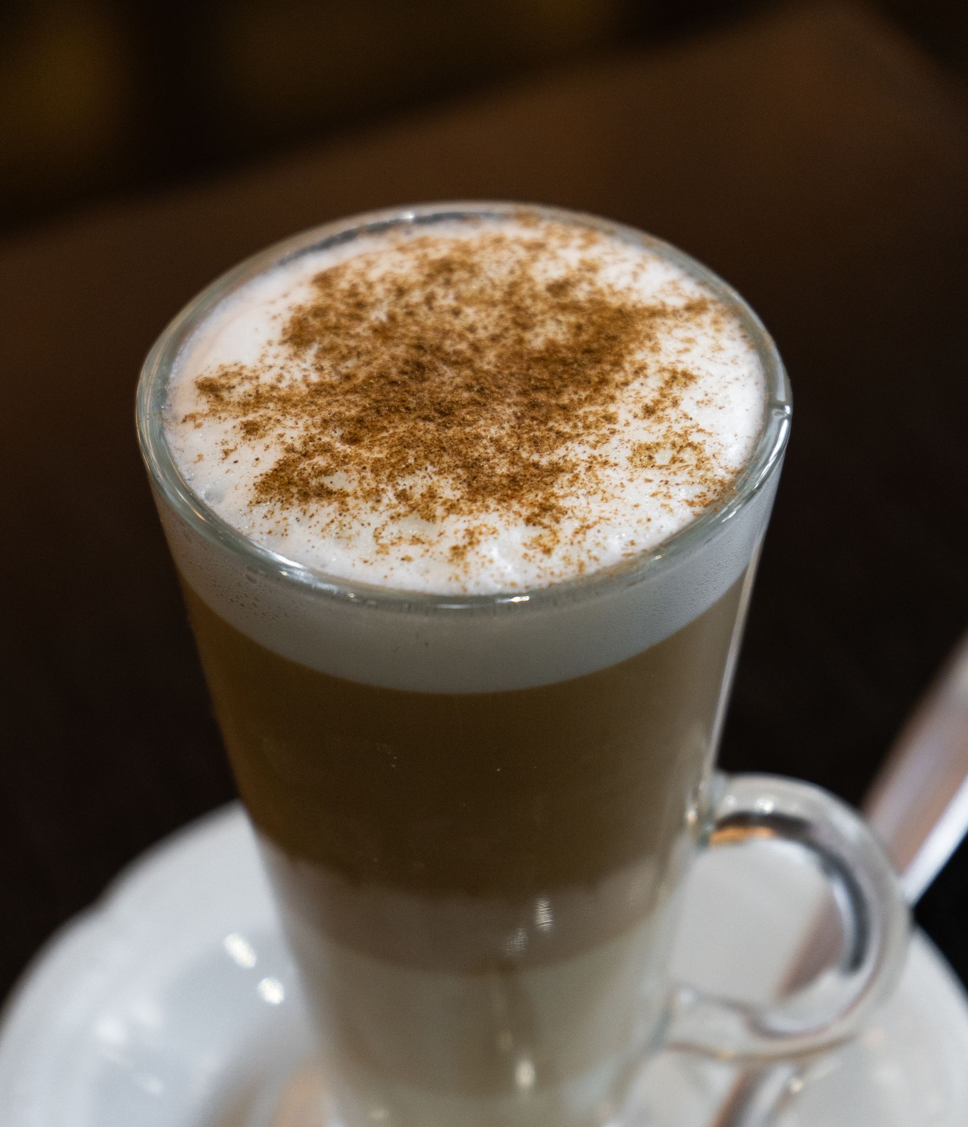 Café con leche en capas en un vaso transparente, cubierto con espuma y canela.