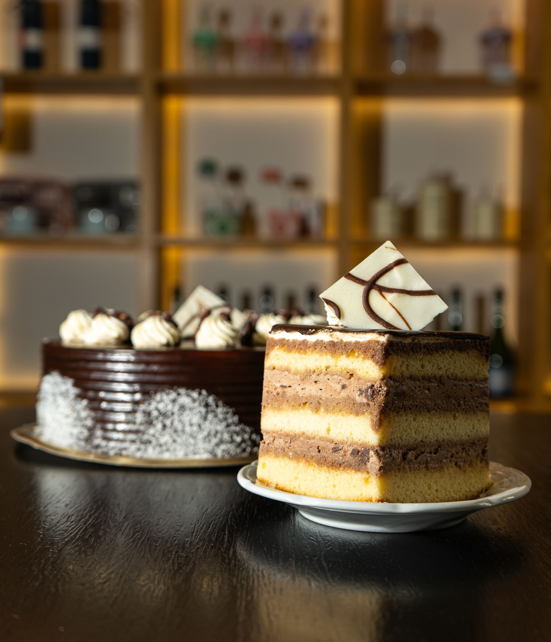 Dos pasteles de chocolate, uno con glaseado y cobertura, el otro en capas, se encuentran sobre una mesa