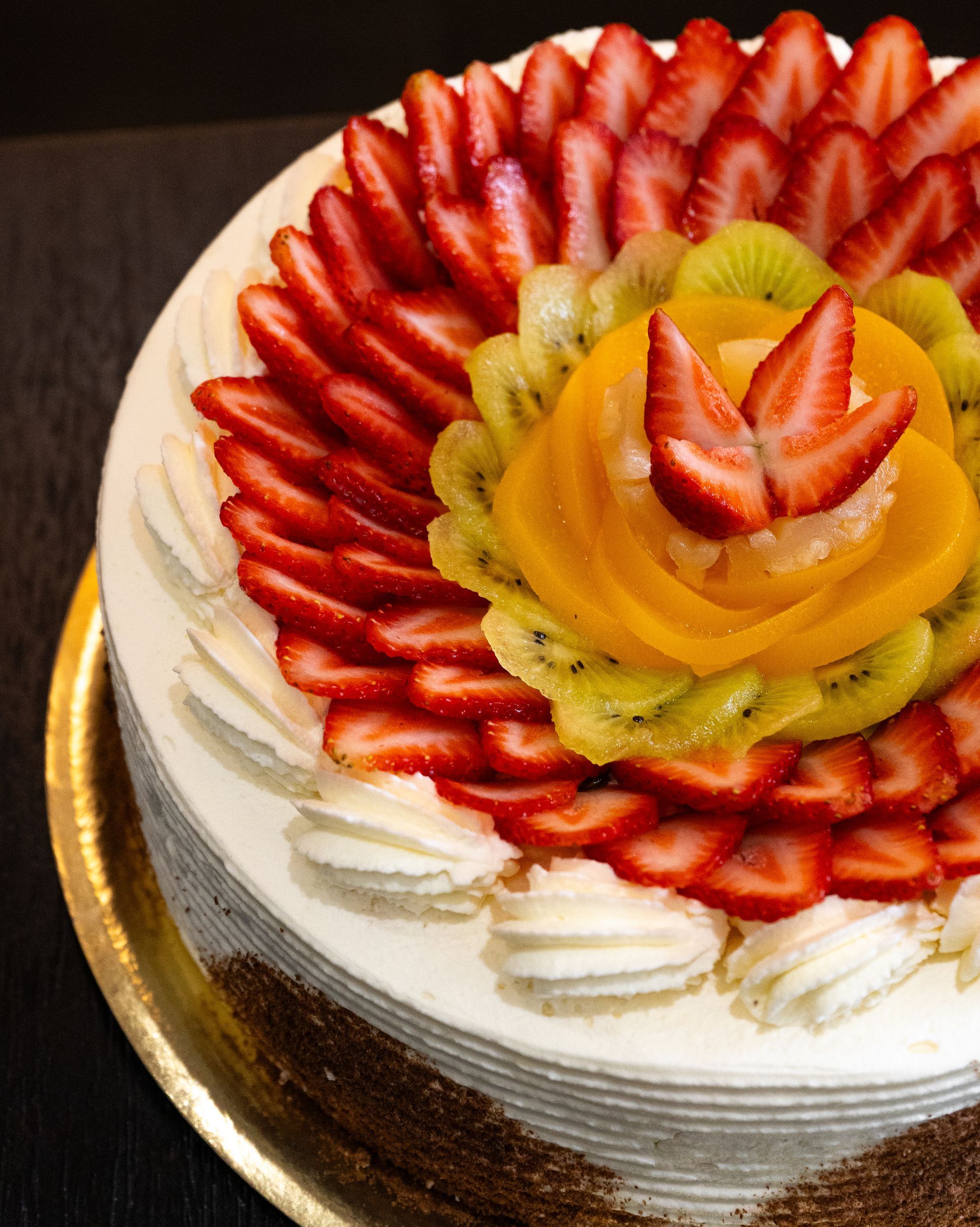 Pastel decorado con fresas, kiwi y rodajas de durazno, cubierto con crema batida.