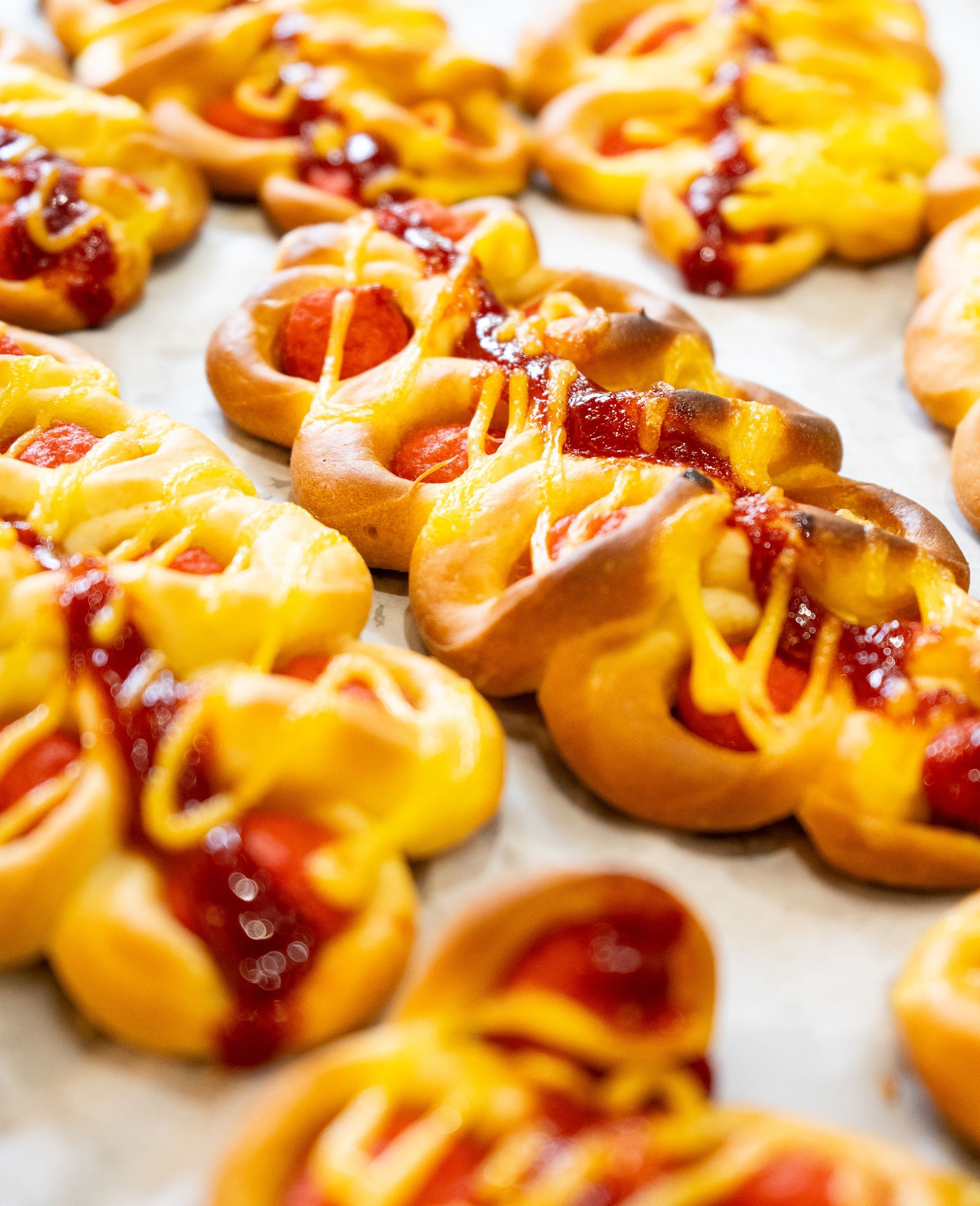 Filas de panecillos horneados cubiertos con salchichas, ketchup y mostaza.