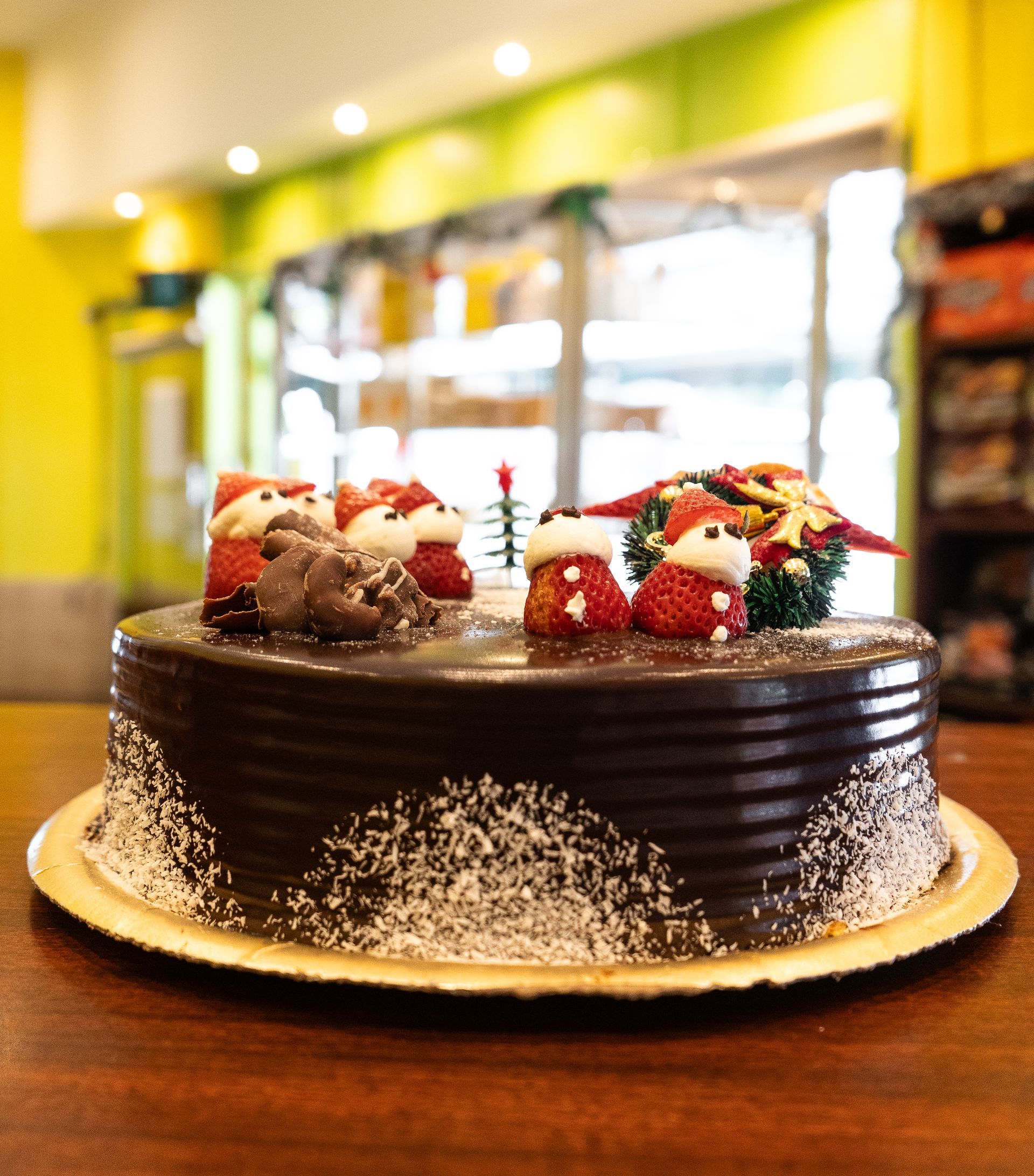 Pastel de chocolate decorado con figuras de Papá Noel y coco, expuesto en un entorno de panadería.
