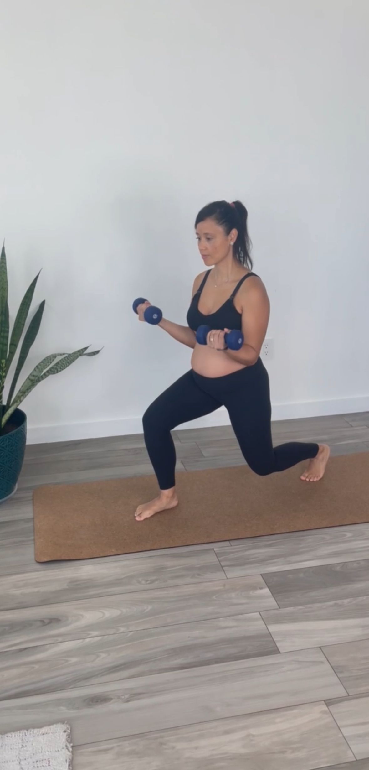 A woman is doing lunges with dumbbells on a yoga mat.