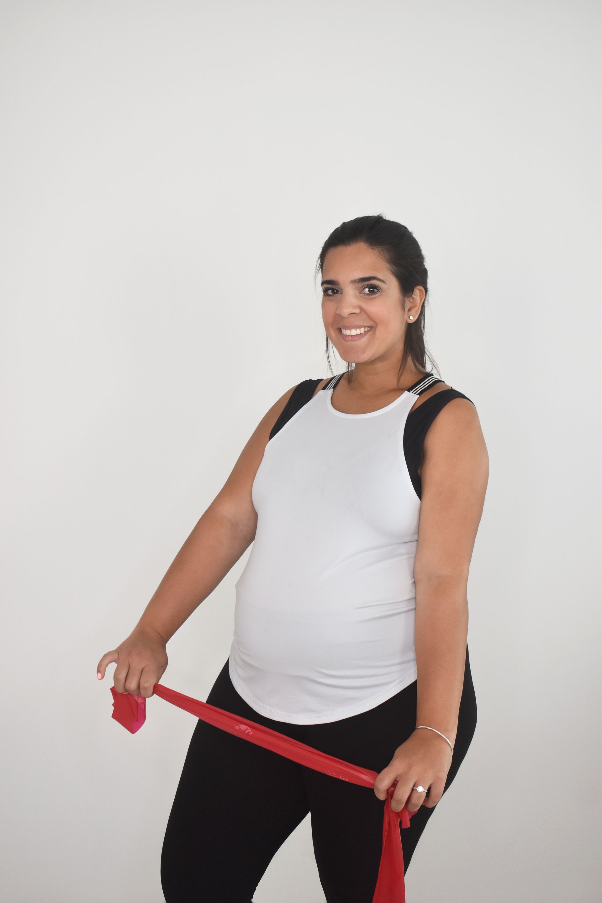A pregnant woman is holding a red resistance band.