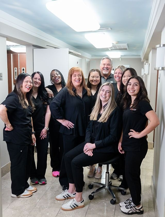 Group of smiling staff in black scrubs posing together in a hospital hallway
