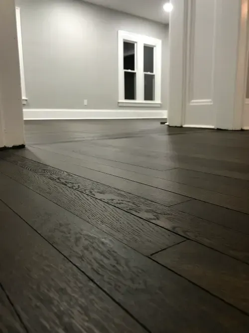 A dark wooden floor in an empty room with a window.