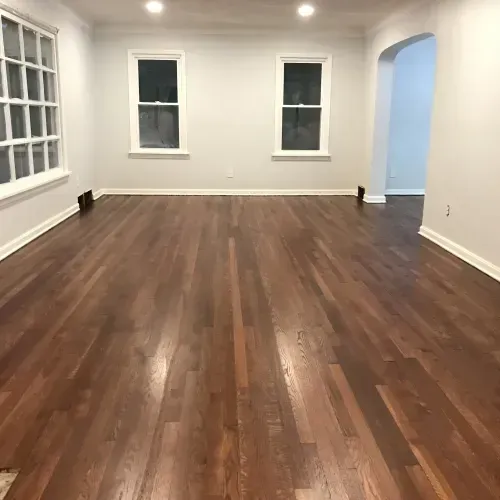 A living room with hardwood floors and two windows.
