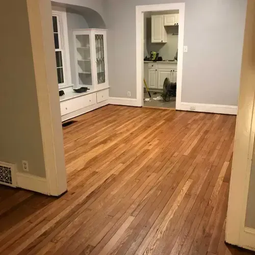A living room with hardwood floors and a kitchen in the background.