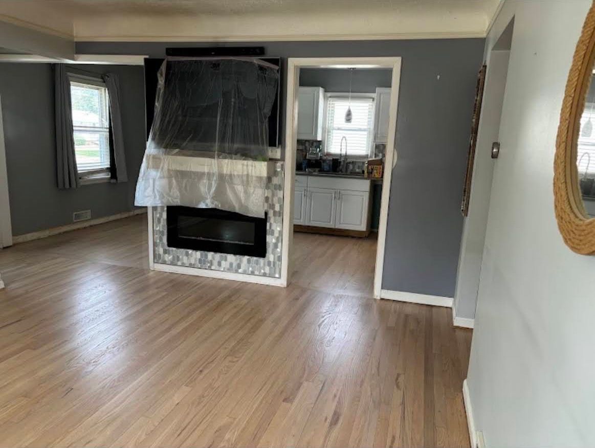 Empty living room with wood floors, gray walls, and a fireplace centered in the space.
