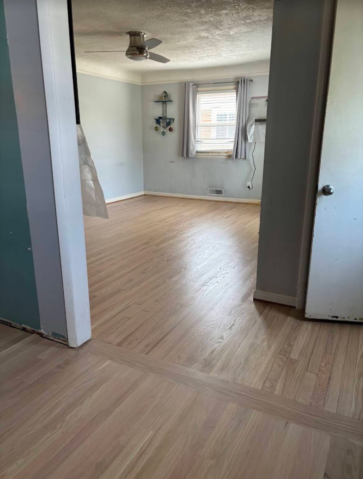 Empty room with light wood floors, pale blue walls, a window, and a ceiling fan.