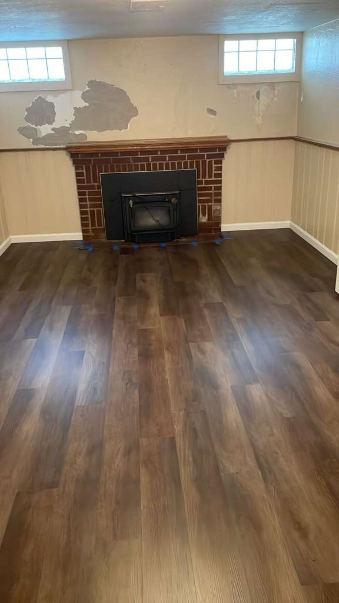 Empty room with wood floor, damaged white walls, brick fireplace, and a small window above the mantel