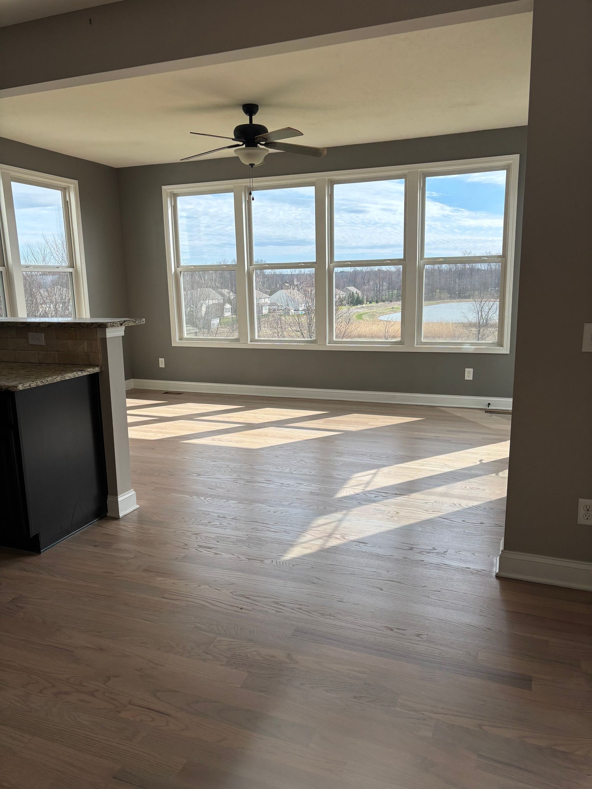 Empty living room with large windows, hardwood floors, and sunlight streaming in, overlooking a city view