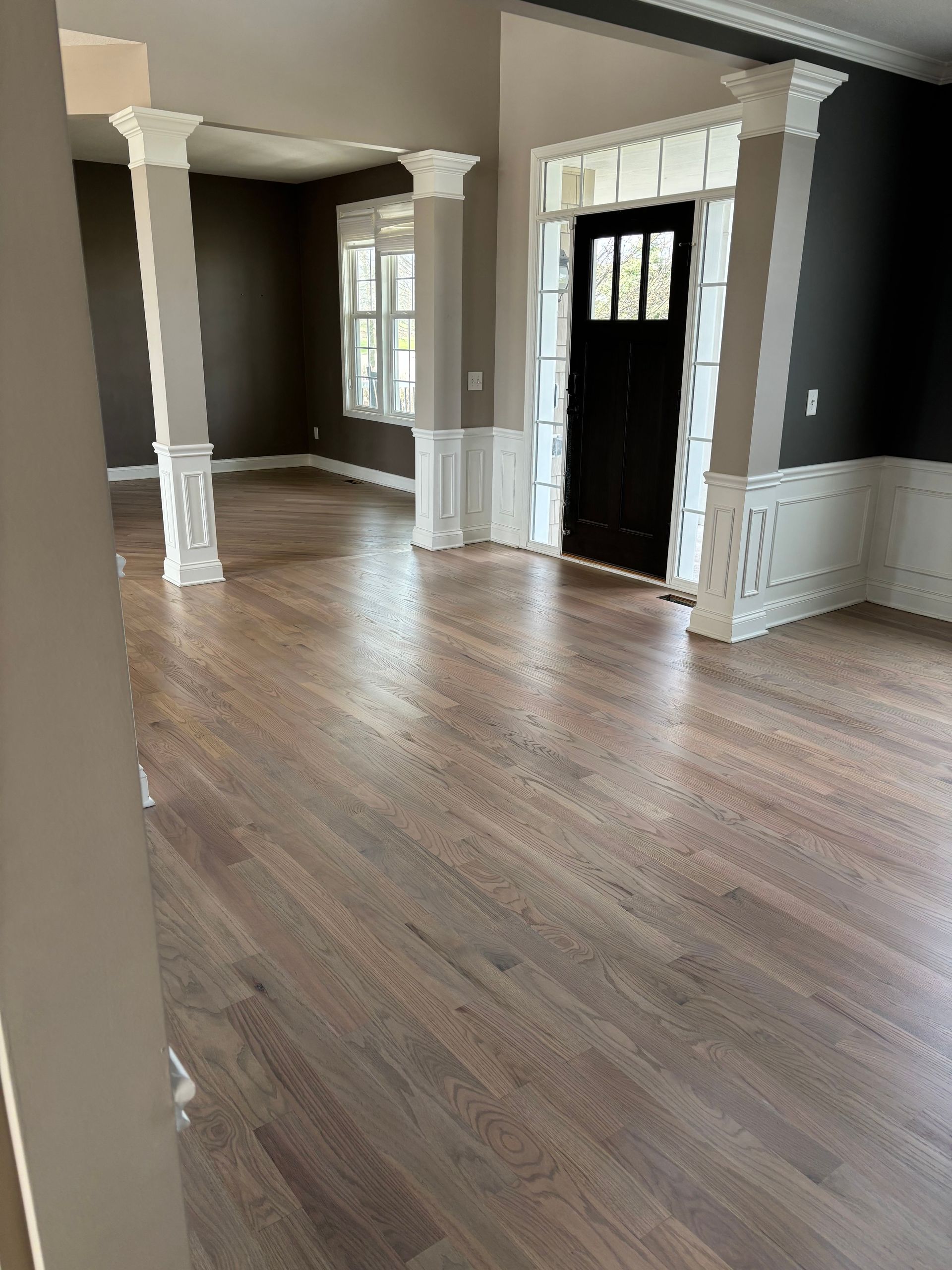 Empty room with hardwood floors, gray walls, white trim, and a black front door