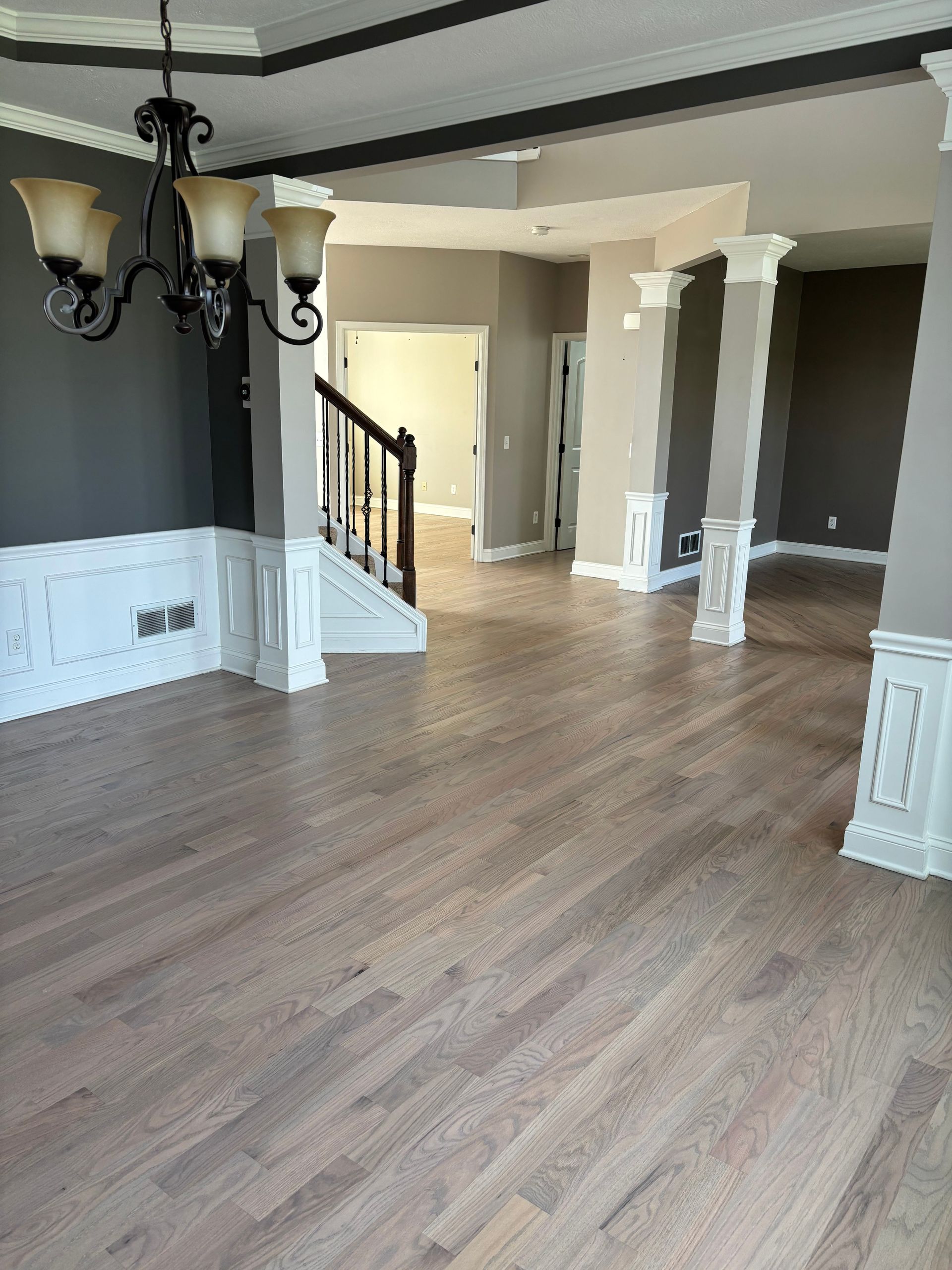 Empty living room with hardwood floors, dark gray walls, white trim, and a chandelier.