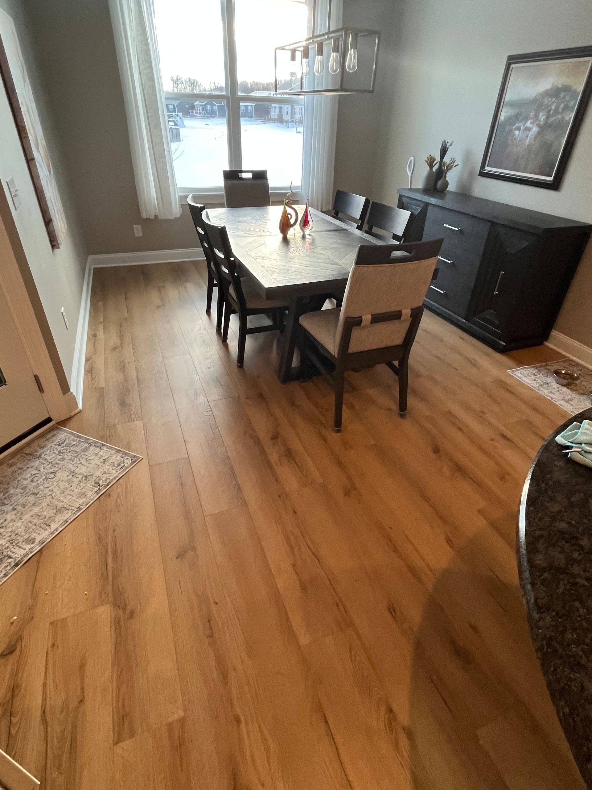Dining room with a wooden table, four chairs, and a sideboard on hardwood floors near a bright window.