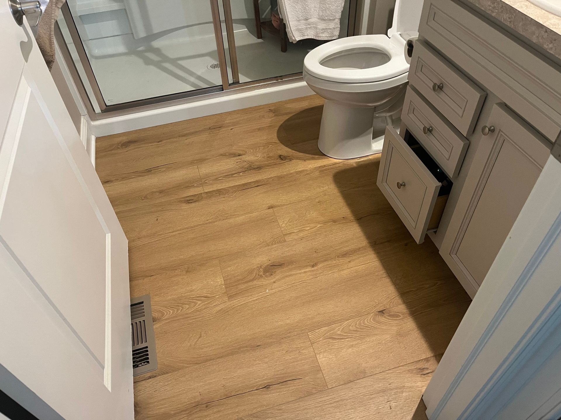 Small bathroom with wood flooring, toilet, sink cabinet, and glass shower enclosure.