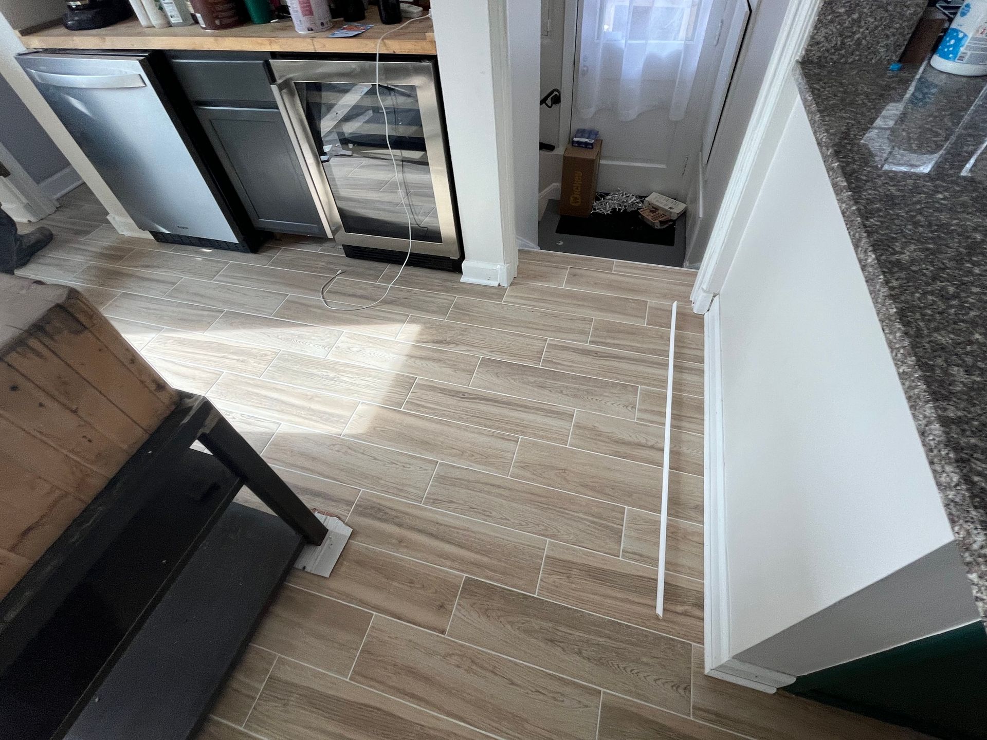 Kitchen floor with light wood planks, black chair, cabinets, and a white appliance near a sunlit doorway