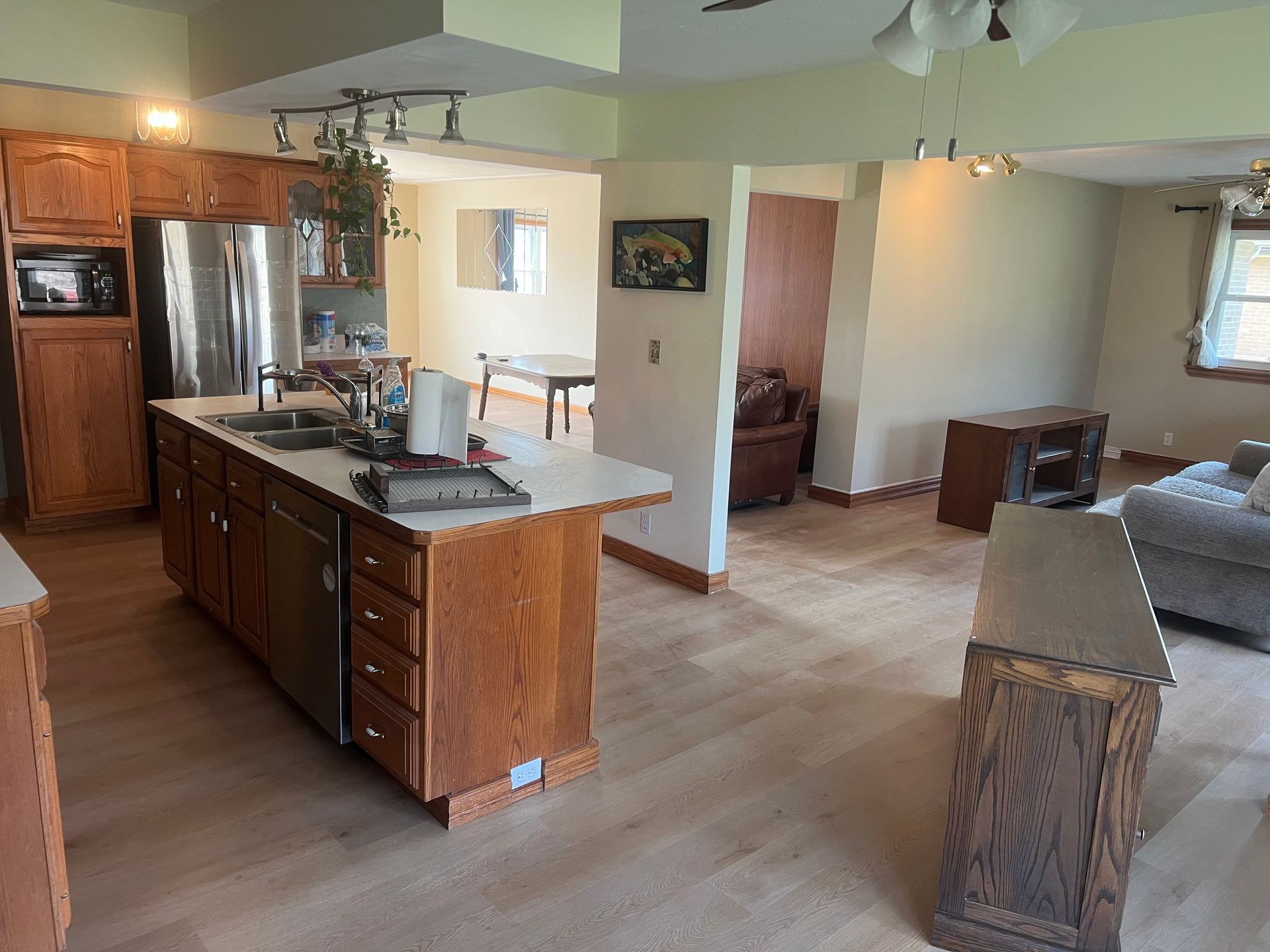 Open-plan kitchen and living room with wood cabinets, island, hardwood floors, and gray sofa.