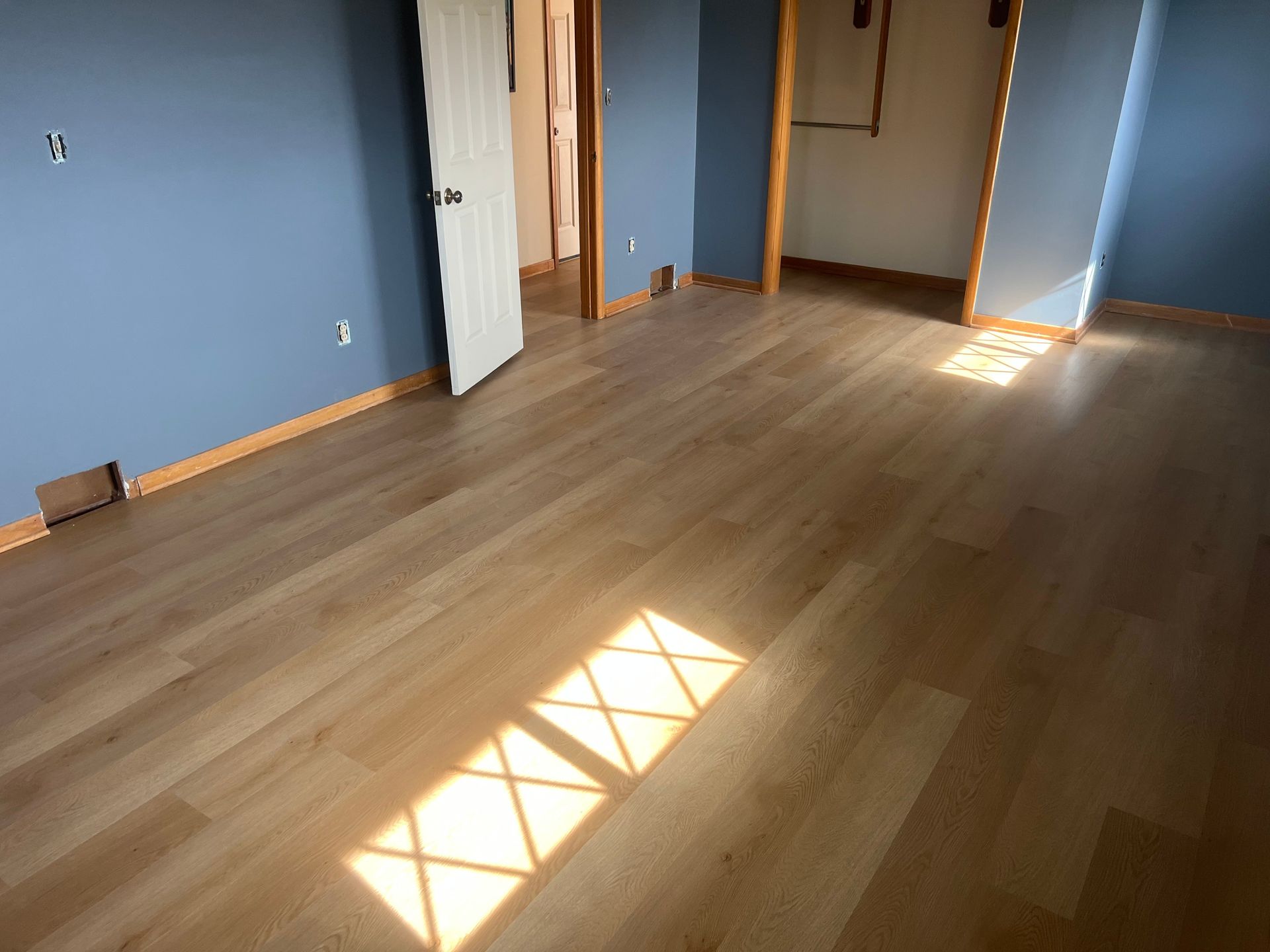 Empty room with blue walls, wood floor, and sunlight streaming through a window.