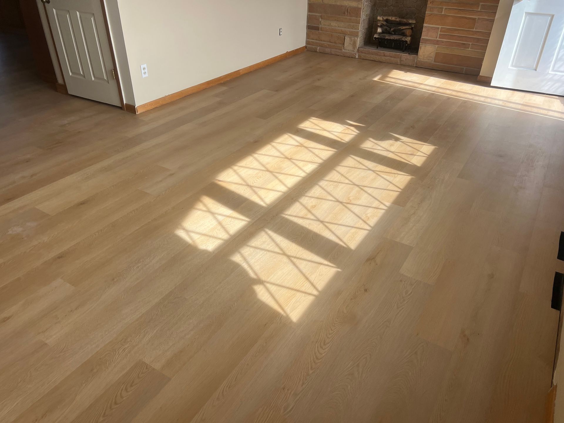 Sunlit empty hardwood living room with window shadows on the floor