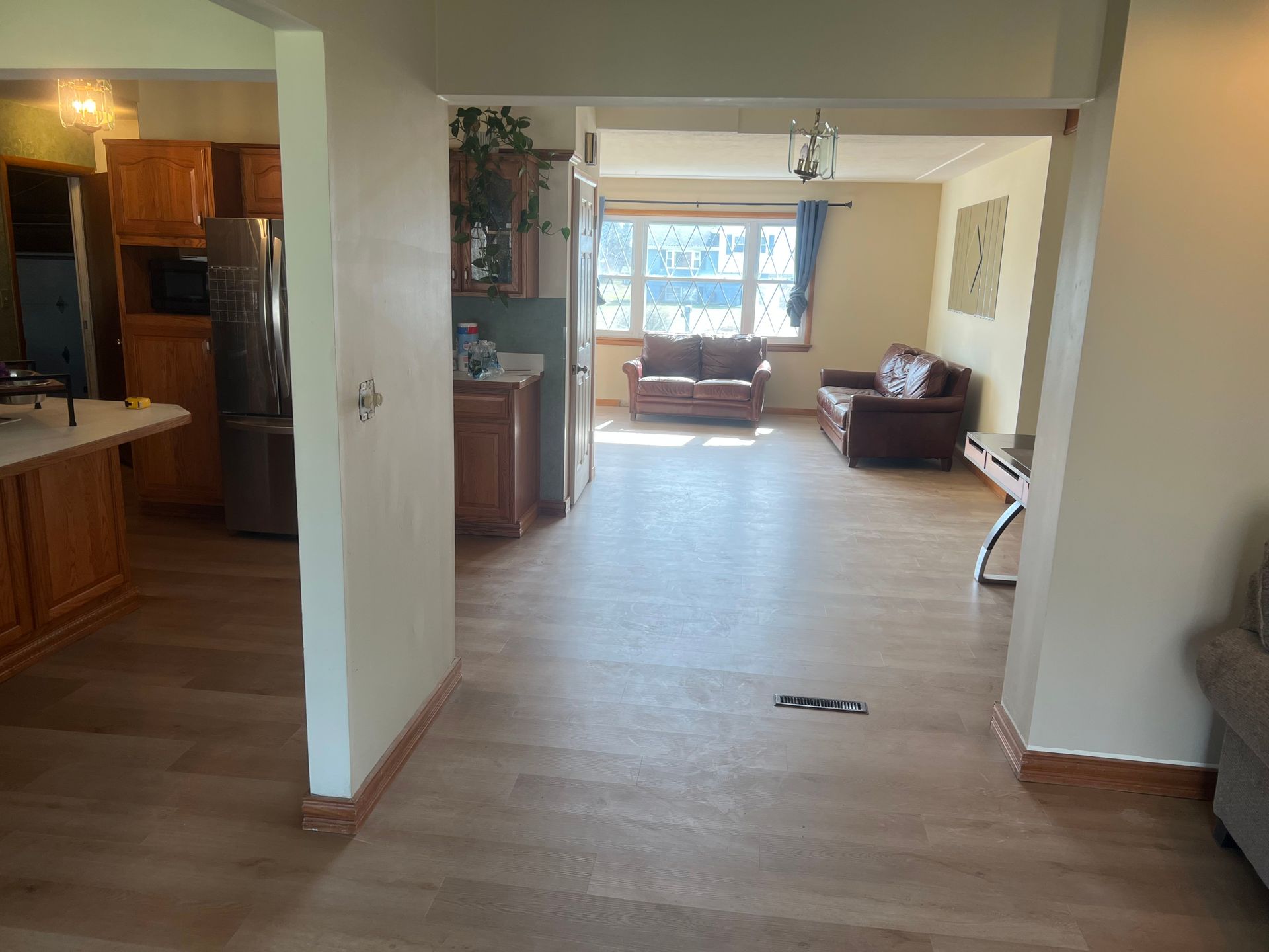 Bright living room and kitchen interior with light walls, wood floors, and a couch by a front window.