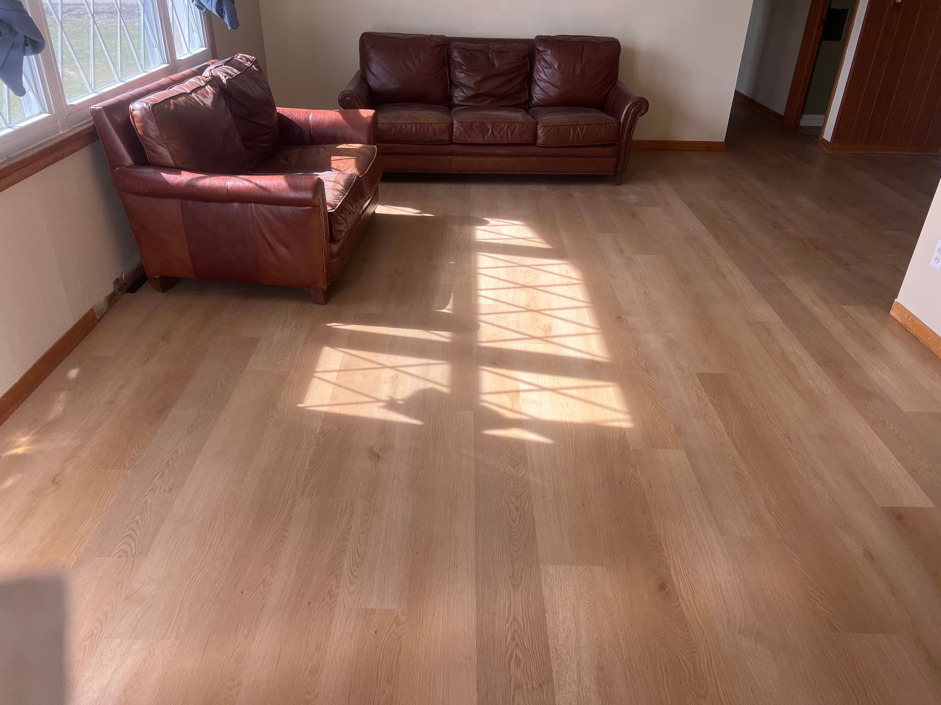 Empty sunlit living room with wood floor and two brown leather sofas along the wall