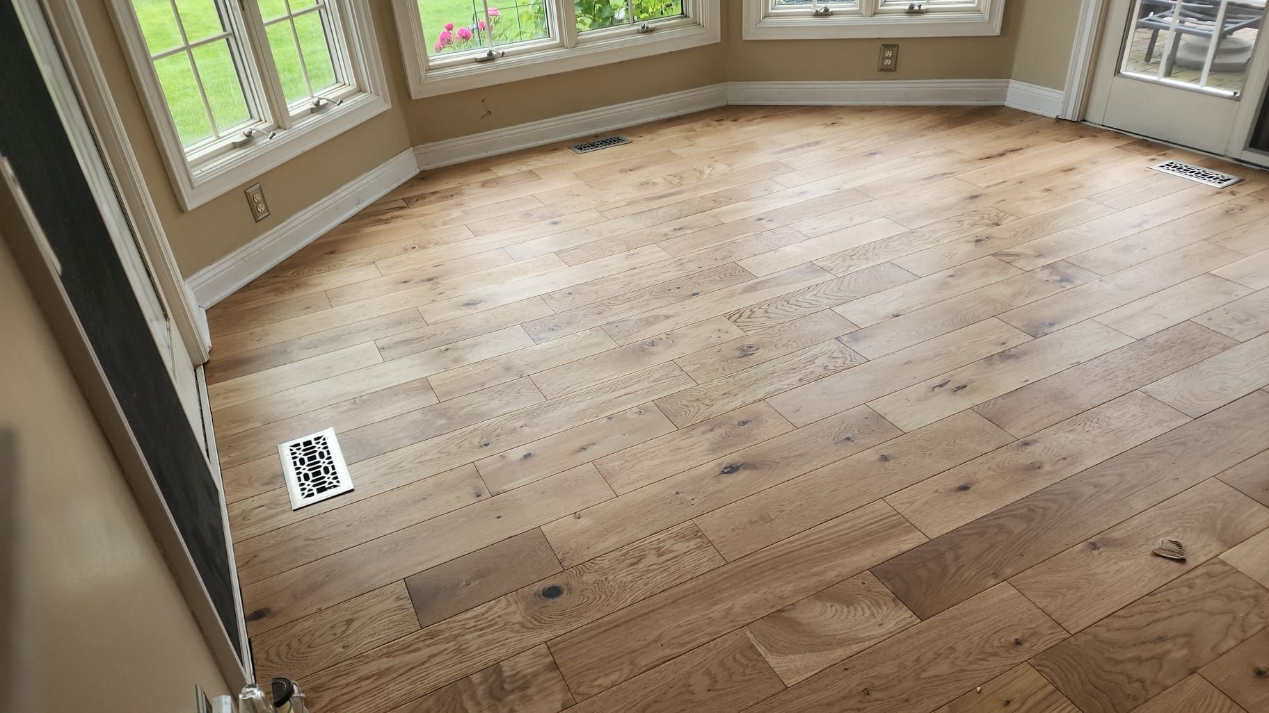 Hardwood floor in a room with multiple windows, sunlight, and a vent.