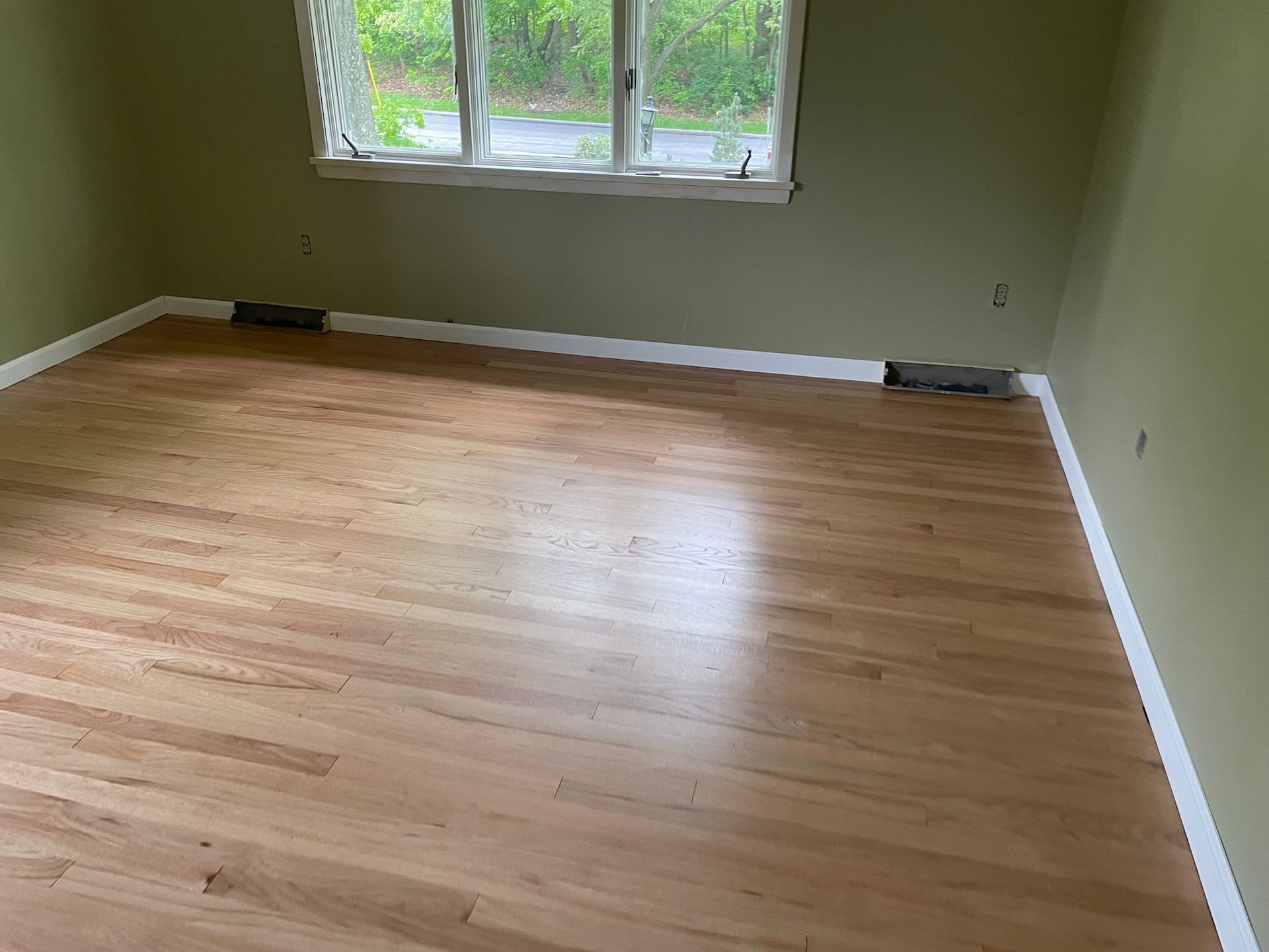 Empty room with hardwood floors, green walls, a white trim, and a window.