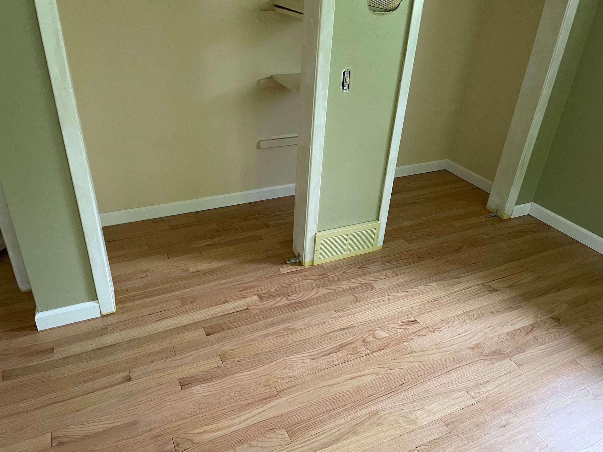 Empty room with light wood floor and open closet with built-in shelves.