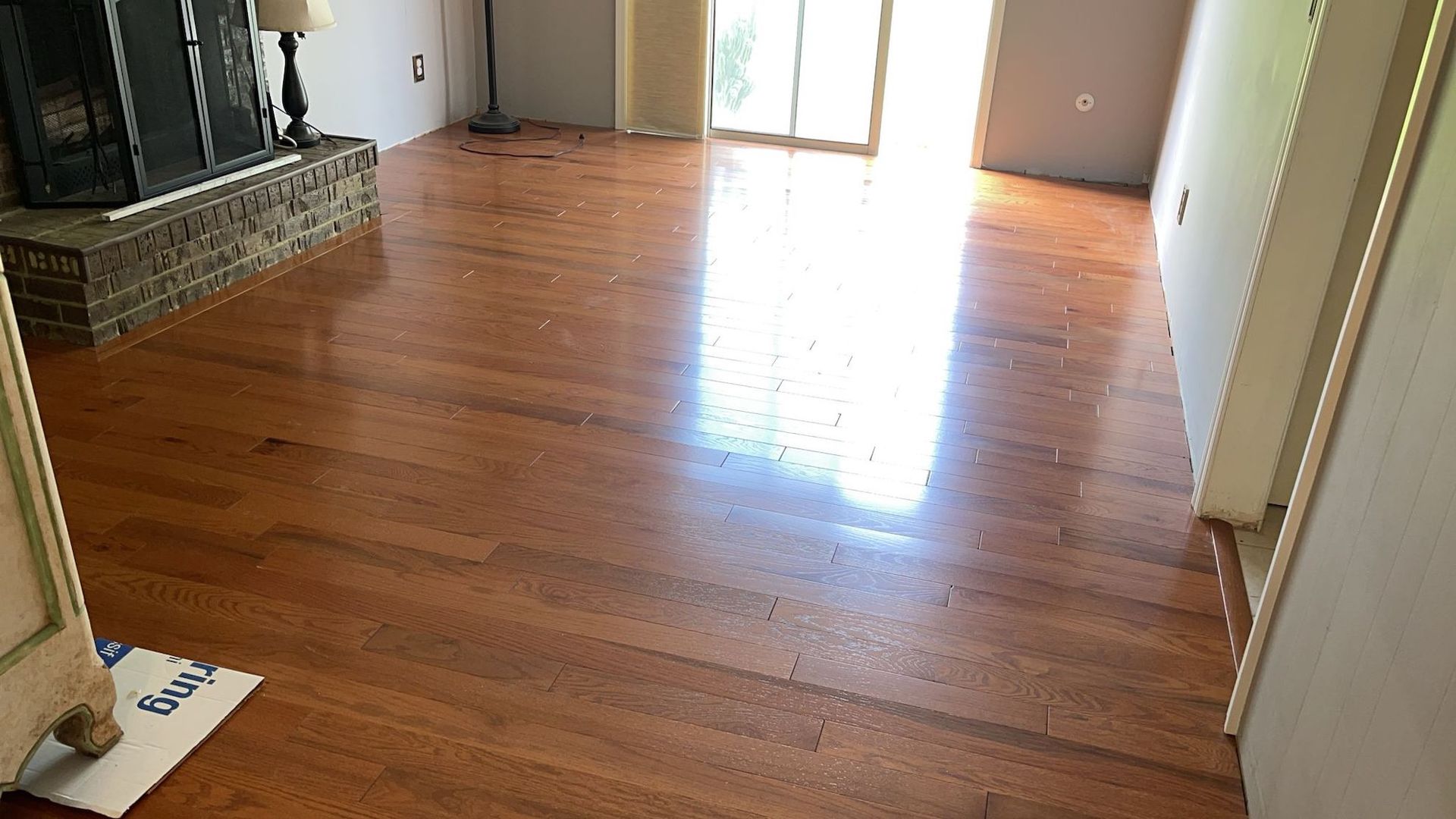 Shiny wood floors in a room with a brick fireplace and sliding glass door.